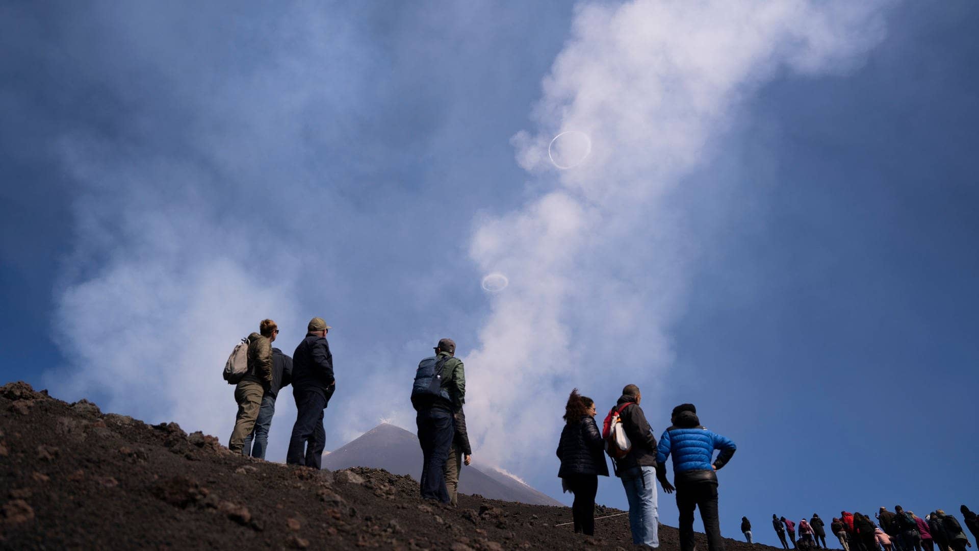 Menschen schauen zu, wie der Vulkan Ätna in Sizilien Ringe aus Rauch in den Himmel spuckt.