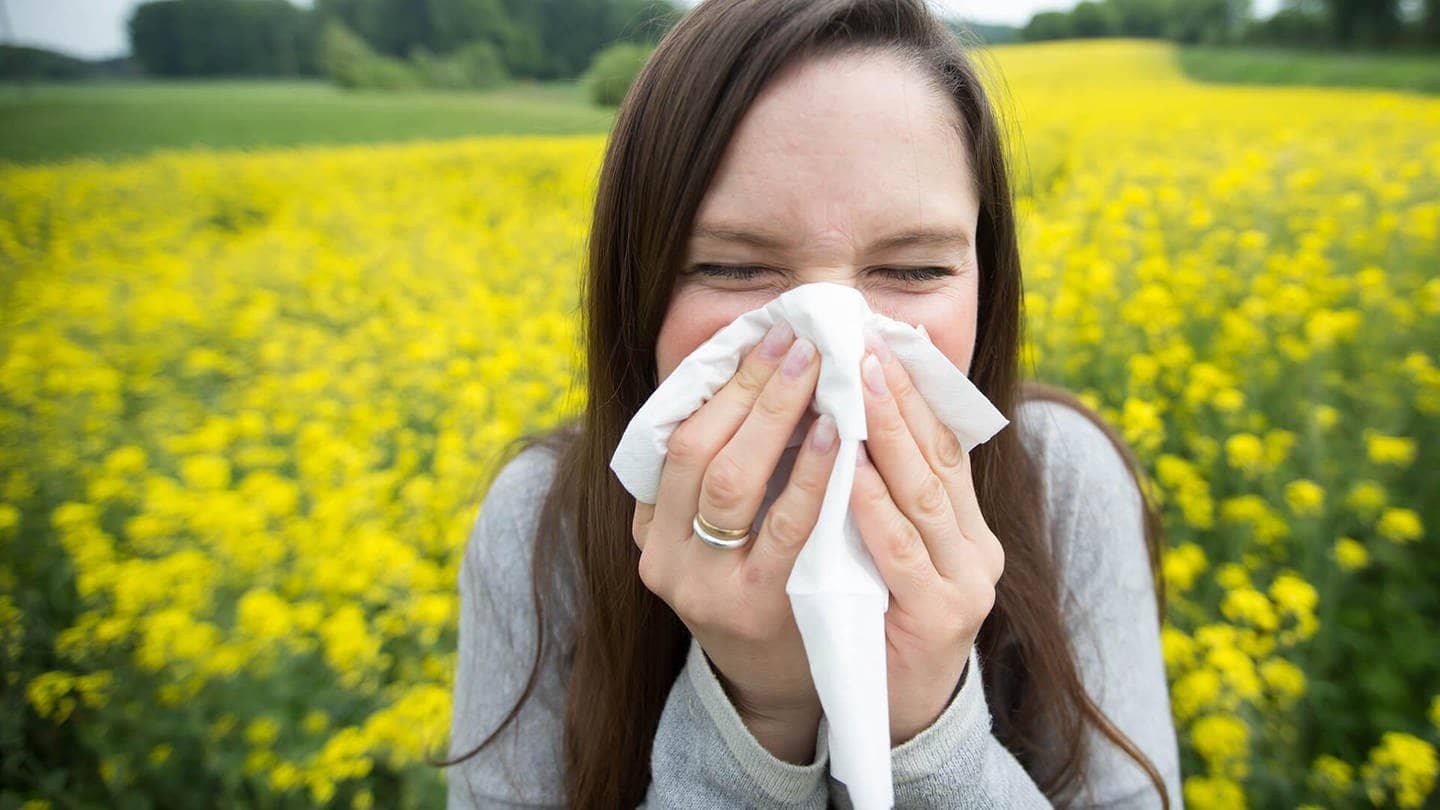 Pollen sind lästig – junge Frau mit Allergie putzt sich die Nase