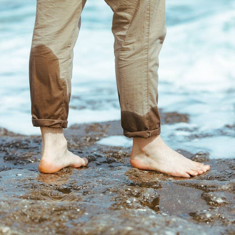 Mann mit halbnassen Hosenbeinen steht im Wasser