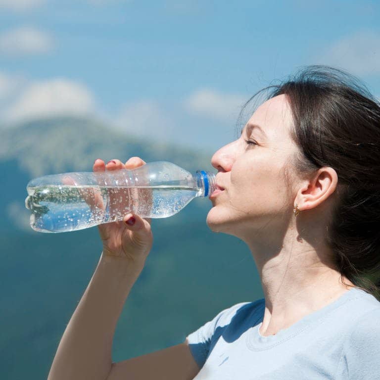 Frau trinkt Wasser vorm Hintergrund der Berge