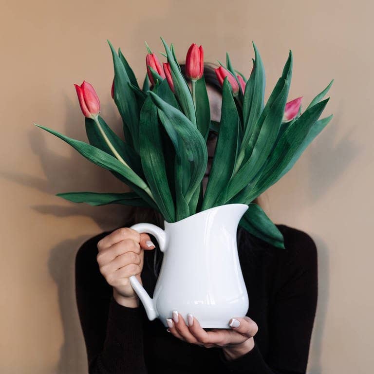Eine Frau hält rote Tulpen in einer Vase vor ihr Gesicht, das Menschen mit Rot-Grün-Schwäche nicht so deutliche erkennen werden