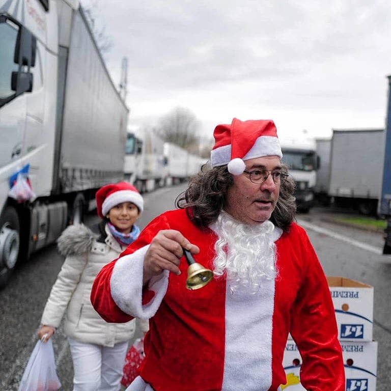 Juan Pedro Garcia Rosales in Weihnachtsmannkostüm klingelt mit einem Glöckchen auf dem Parkplatz zwischen Lkws.