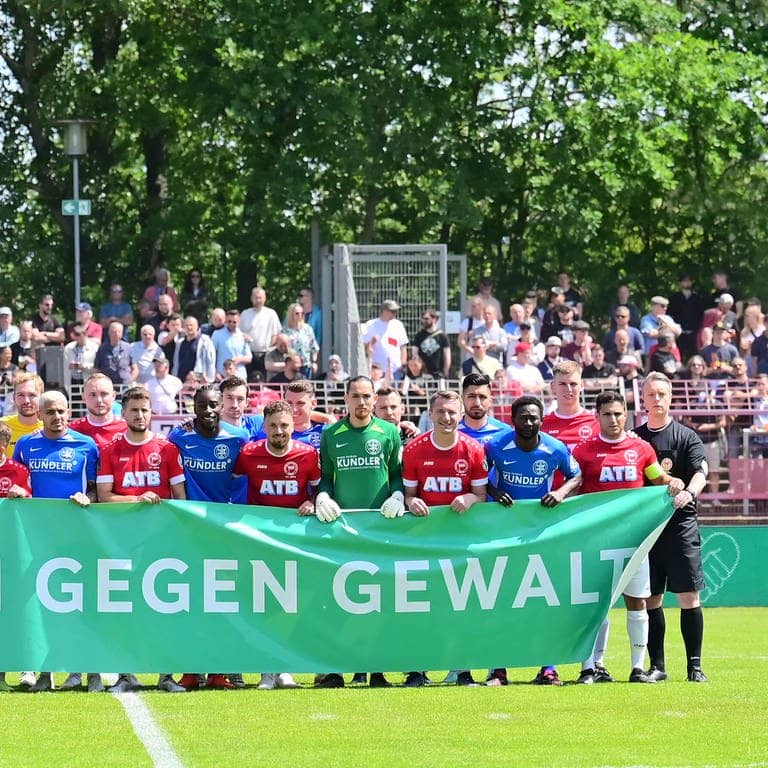 Die Spieler der Mannschaften TuS Makkabi und SV Sparta Lichtenberg halten vor dem Spiel ein Transparent mit der Aufschrift "Gemeinsam gegen Gewalt" in den Händen.