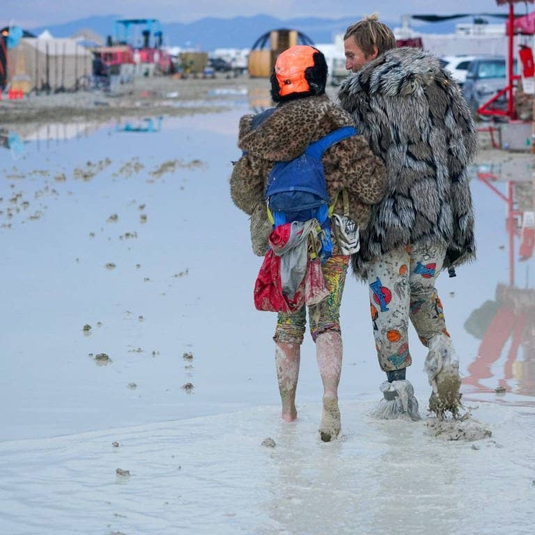Ein verkleidetes Pärchen läuft durch eine große Pfütze beim Burning Man Festival