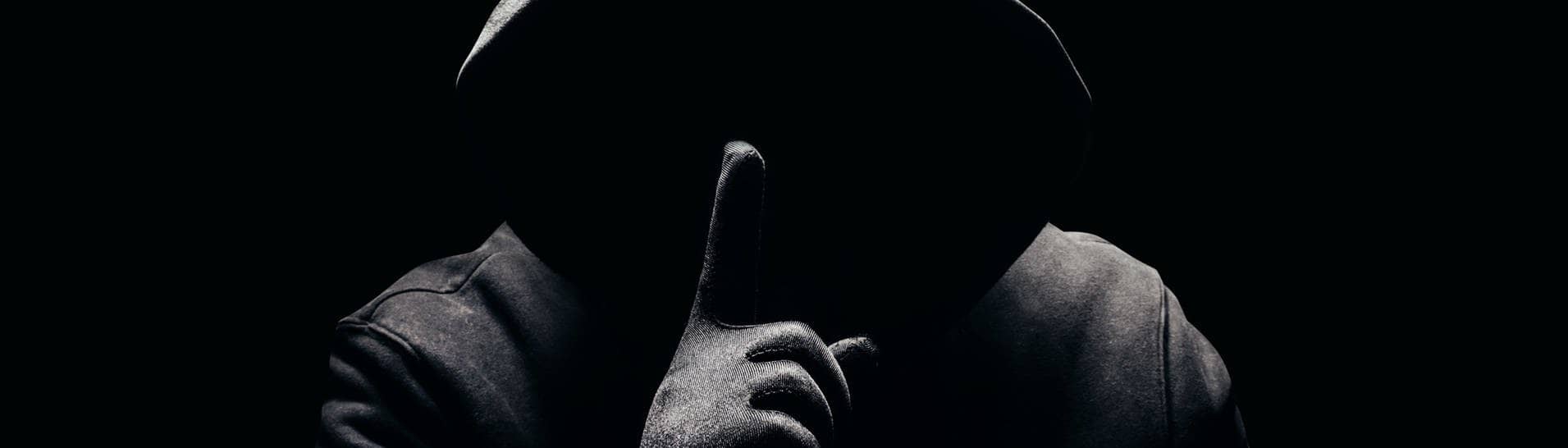 Eine dunkle Person, ohne Gesicht hält den Finger als Aufforderung zur Verschwiegenheit vor den Mund. Symbolbild für „Wie böse bin ich“-Selbsttest.