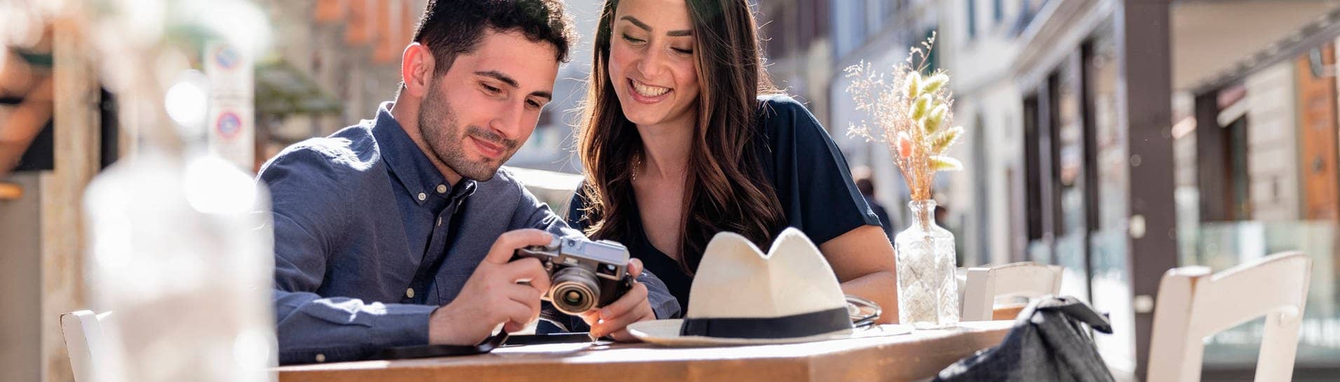 Ein Pärchen Touristen beim Städtetrip. Sie schauen sich Fotos auf einer Kamera an und sitzen in einem Café einer Stadt .