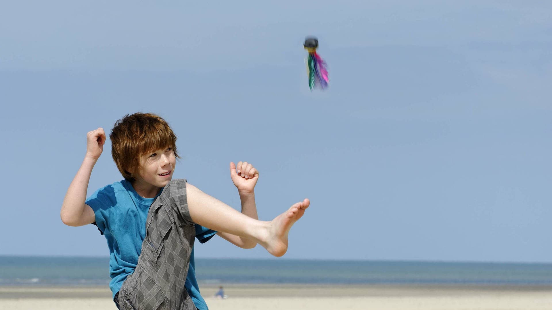 Junge kickt Indiaca-Ball an einem Strand in die Luft