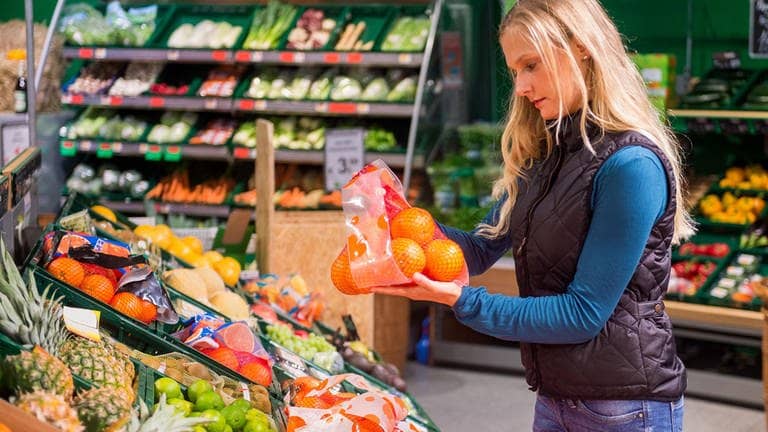 Eine Frau vergleicht in einem Supermarkt ein Netz Orangen