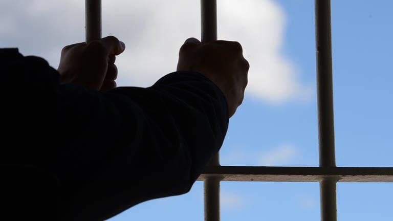 Ein Mann hält die Gitterstäbe einer Gefängniszelle fest