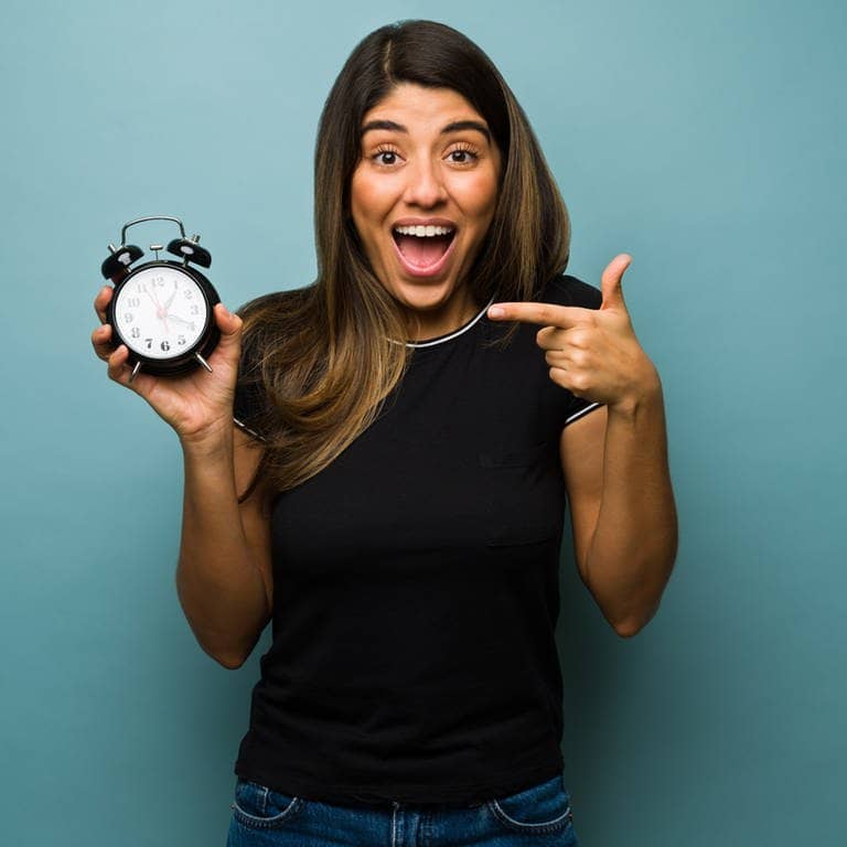 Eine Frau hält eine Uhr in der Hand und macht einen überraschten Gesichtsausdruck, weil die Zeitumstellung ist (Foto: Adobe Stock, AntonioDiaz)