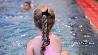 Ein Mädchen sitzt im Badeanzug am Beckenrand und nimmt an einem Schwimmkurs teil. 