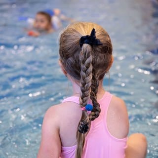 Ein Mädchen sitzt im Badeanzug am Beckenrand und nimmt an einem Schwimmkurs teil. 