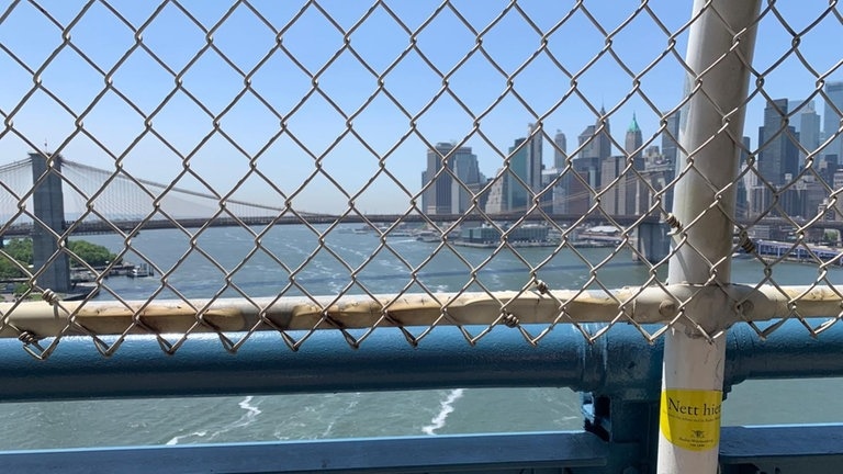 Der Sticker "Nett hier aber waren Sie schon mal in Baden-Württenberg" klebt an einem Geländer auf der Brooklyn Bridge in New York.