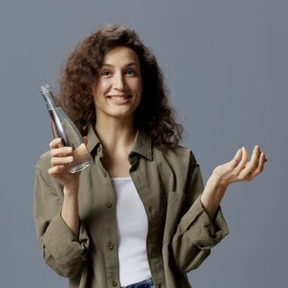 Frau hält ein Glas mit Leitungswasser in der Hand und fragt sich, welche Mythen stimmen.