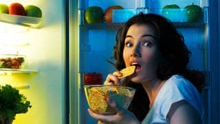 Frau isst salzigen Keks, vor offenem Kühlschrank 