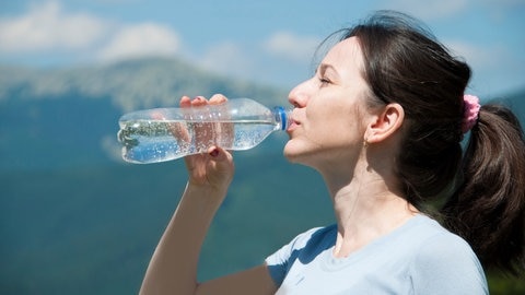 Frau trinkt Wasser vorm Hintergrund der Berge