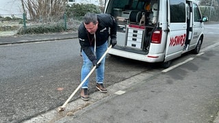 SWR3 Reporter und Glücksbringer Josh Kochhan in Pirmasens, wie er einen Gehweg von trockenem Gras befreit.