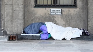 Obdachlose Person liegt vor Gebäude