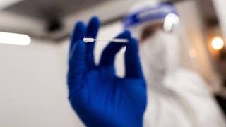 Medizinisches Personal mit Stäbchen für Corona-Test in der Hand