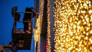 Ein Mann hängt am Königsbau in Stuttgart (Baden-Württemberg) von einer Hebebühne Weihnachtsbeleuchtung auf.