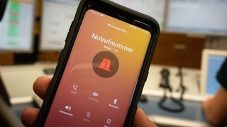 Ein Handy, auf dem vor orangefarbenem Grund die Notrufunummer 112 gewählt wird