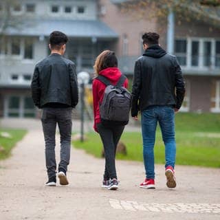 Drei Jugendliche gehen über das Gelände einer Schule.