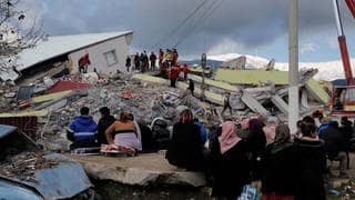 Menschen sitzen vor einem eingestürzten Gebäude in Gaziantep.