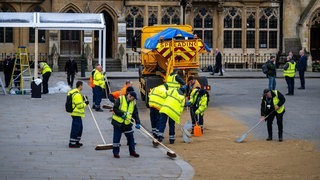 Die Straße vor der Westminster Abbey wird für die Ankunft des Königs vorbereitet. Mitarbeiter der Strassenreinigung putzen die Straße.