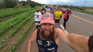 Jonas Deichmann, deutscher Extremsportler, fotografiert sich während seines Triathlons um die Welt selbst. Im Hintergrund Anhänger, die mit ihm ein Stück laufen. 