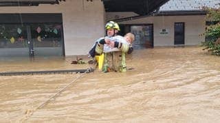 Feuerwehrmann Sandi Zajc trägt ein Kind aus einem überfluteten Kindergarten