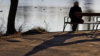 Eine Frau sitzt alleine auf einer Bank an einem See