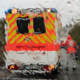 (Symbolbild) Im strömenden Regen geht ein Notfallsanitäter des Deutschen Roten Kreuzes (DRK) zu einem Rettungswagen, der vor dem Haus eines Patienten steht. 