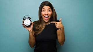 Eine Frau hält eine Uhr in der Hand und macht einen überraschten Gesichtsausdruck, weil die Zeitumstellung ist
