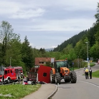 Rettungskräfte stehen nach einem Unfall neben einem einem umgestürzten Maiwagen. Bei dem Unfall mit einem Maiwagen-Anhänger sind im südbadischen Kandern rund dreißig Menschen verletzt worden. Zehn Menschen hätten schwere Verletzungen erlitten, teilte die Polizei am Mittwoch mit.