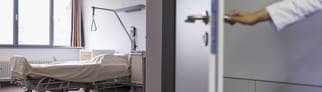 Eine Hand öffnet eine Tür zu einem leeren Bett in einem Krankenzimmer in einem Krankenhaus