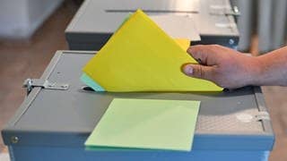 Eine Person steckt seine Stimmzettel zur Kommunalwahl in eine Wahlurne.