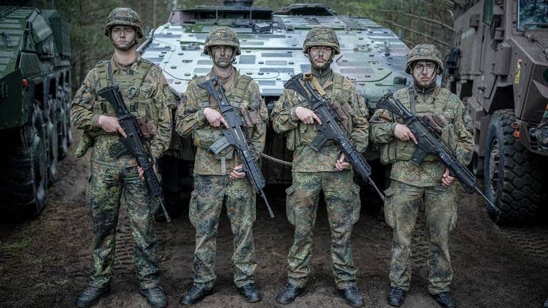 Vier Soldaten der Bundeswehr stehen mit Tarnschminke bemalten Gesichtern vor einem Panzer.