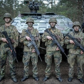 Vier Soldaten der Bundeswehr stehen mit Tarnschminke bemalten Gesichtern vor einem Panzer.