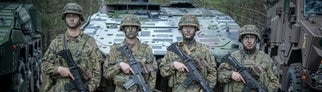 Vier Soldaten der Bundeswehr stehen mit Tarnschminke bemalten Gesichtern vor einem Panzer.