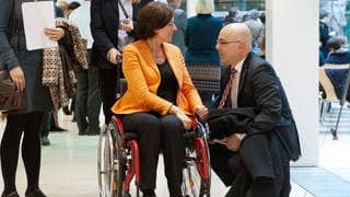 Malu Dreyer sitzt in einem Rollstuhl und unterhält sich mit dem schleswig-holsteinischen Ministerpräsidenten Torsten Albig, der vor ihr kniet.