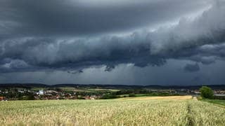 Eine Gewitterzelle mit dunklen Wolken baut sich am Himmel und hinter Feldern nahe Heilbronn auf. 
