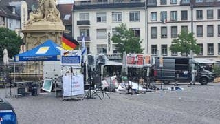 Überreste des Stands der Bürgerbewegung „Pax Europa“ auf dem Mannheimer Marktplatz nach einer Messerattacke; im Hintergrund ein Mitarbeiter der Spurensicherung
