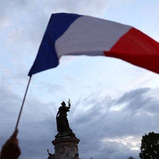 Eine französische Flagge wird vor einer Statue am Place de la Republique in Paris (Frankreich) geschwenkt
