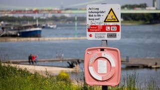 Ein Hinweisschild mit der Aufschrift "Achtung Lebensgefahr" weist am Rhein in Rodenkirchen auf die Gefahren beim Schwimmen in dem Fluss hin.