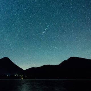 Eine Sternschnuppe leuchtet am 12.08.2018 am Himmel über dem Walchensee (Archiv).