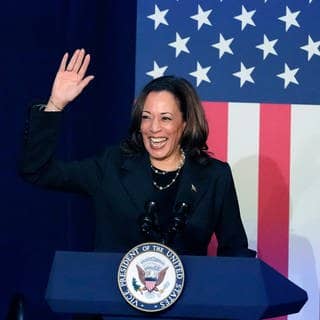 Kamala Harris, Vizepräsidentin der USA, lacht und hält ihre rechte Hand hoch