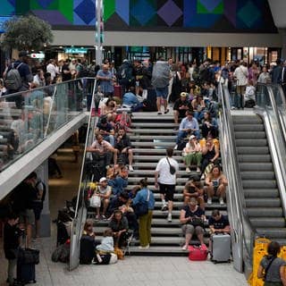 Reisende sitzen auf einer Treppe am Gare de Montparnasse vor den Olympischen Sommerspielen 2024. Wenige Stunden vor der Eröffnung der Olympischen Spiele in Paris haben Unbekannte Brandanschläge auf mehreren Anlagen des französischen Schnellzugnetzes verübt.