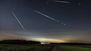 Sternschnuppen in der Nacht über einer Landschaft, hier sind die Perseiden zu beobachten.