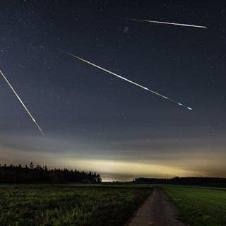 Sternschnuppen in der Nacht über einer Landschaft, hier sind die Perseiden zu beobachten.