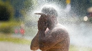 Man sieht einen Mann im Schwimmbad, der mit seiner Baseballkappe duscht.